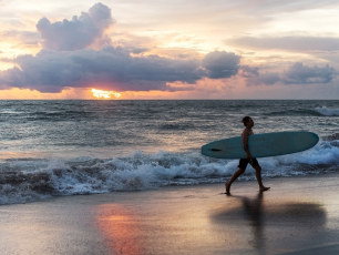 Surfer walking on a beach at sunset