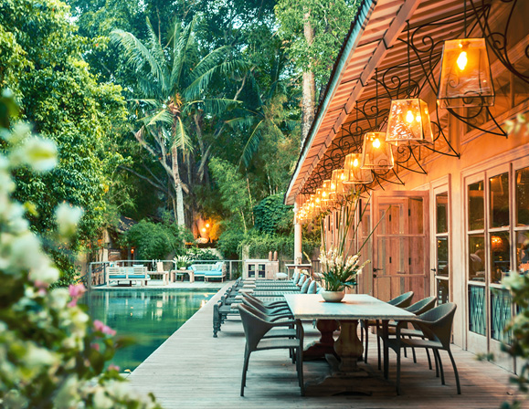 Villa patio with dining table and poolside seating surrounded by greenery