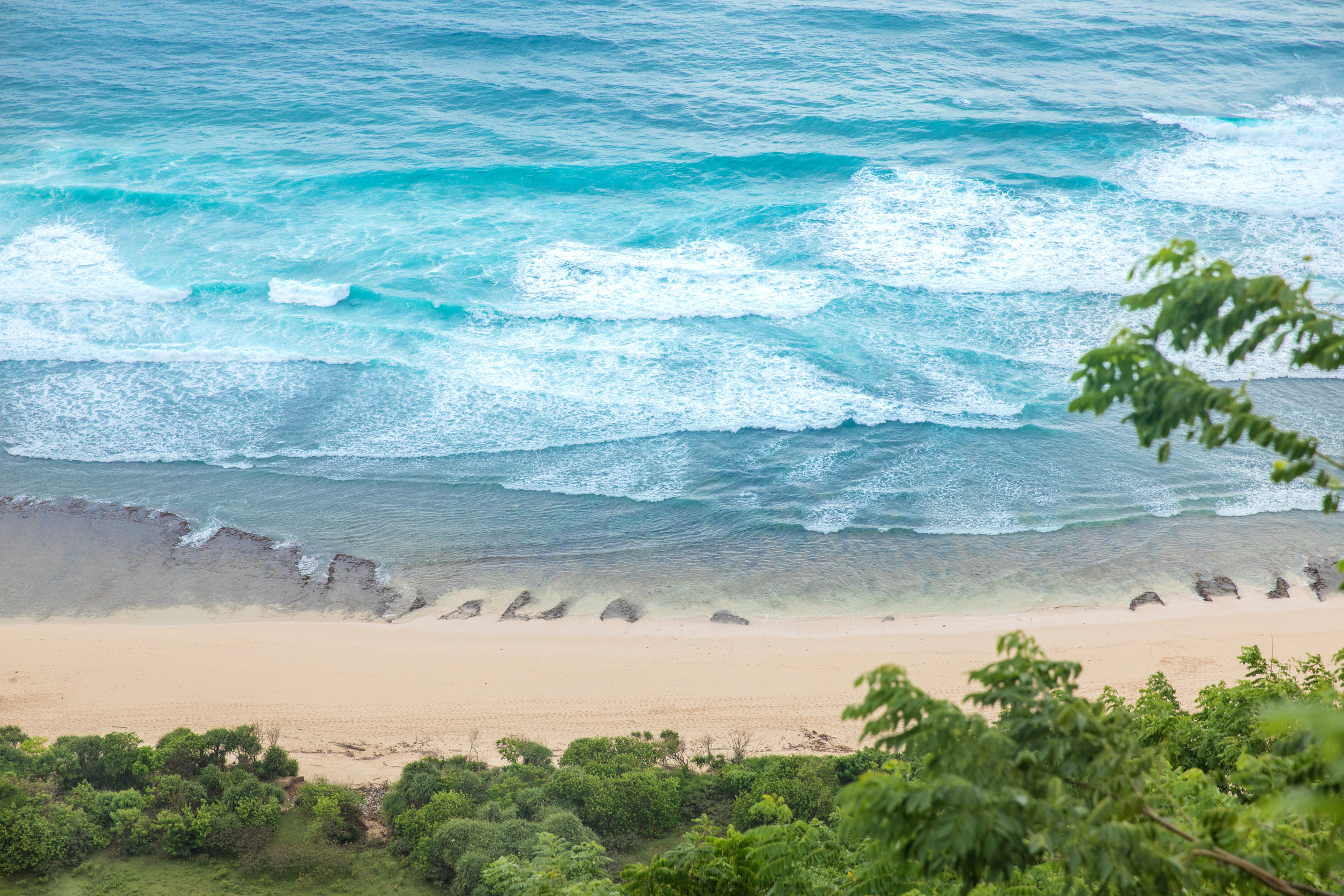 Aerial view of turquoise waves and golden sand with greenery
