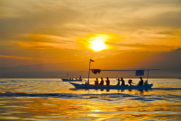 Traditional boat with passengers silhouetted against a golden sunset in Lovina