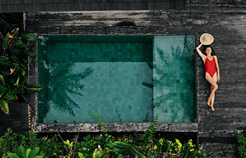 Woman in red swimsuit leaning on a luxury villa pool wall