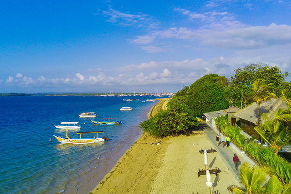 Sanur beach with boats anchored near the shore and a walking path along the coast.