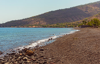 Rocky beach with soft waves and hills in the distance at sunset