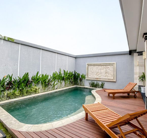 Private villa pool with wooden lounge chairs and lush greenery
